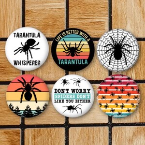 May include: Six round buttons with different spider designs. The buttons have a white background with black spider silhouettes and text. The text on the buttons reads "Tarantula Whisperer", "Life is better with a Tarantula", "Don't worry spiders don't like you either", and "Tarantula".