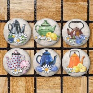 May include: A set of six circular ceramic tiles, each featuring a painted illustration of a different teapot surrounded by flowers and fruit. The teapots are depicted in black, green, brown, white with red dots, blue, and orange colors.