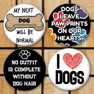 May include: Four circular pin-back buttons featuring dog-themed designs. One white button shows a tan bone with the text MY NEXT DOG WILL BE NORMAL. One black button displays colorful paw prints and the text DOGS LEAVE PAW PRINTS ON OUR HEARTS. One black button features a paw print and the text NO OUTFIT IS COMPLETE WITHOUT DOG HAIR. One white button shows a red heart made of small paw prints and the text I LOVE DOGS.
