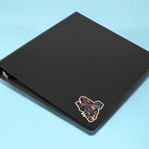 May include: Black binder with a sticker of a cartoon welder holding a welding torch and the text "Weld This!"