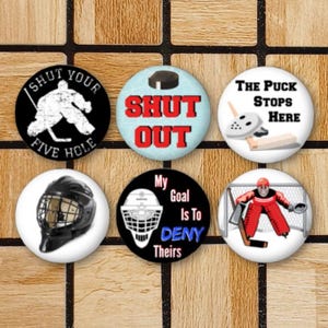 May include: Six round hockey-themed buttons with various designs. The buttons feature hockey players, pucks, and text such as "Shut Out", "The Puck Stops Here", and "My Goal Is To Deny Theirs".