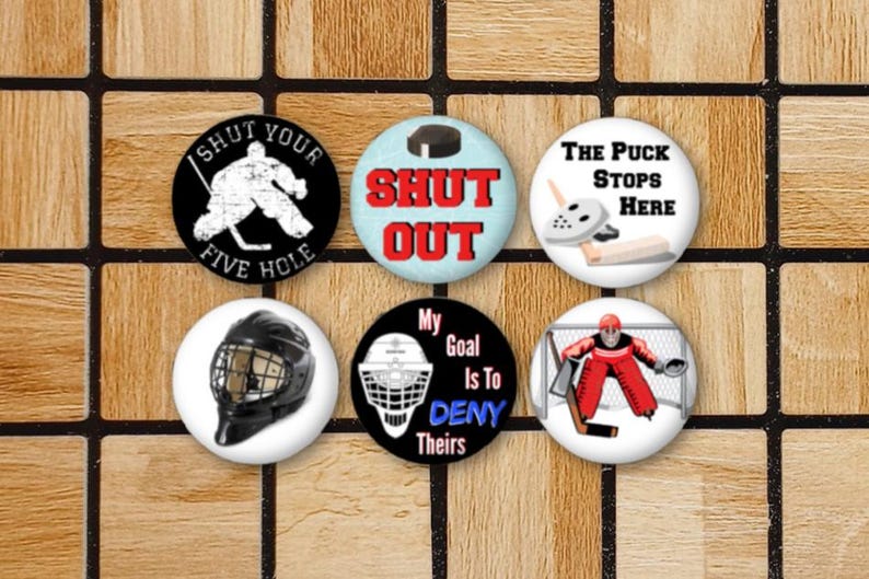 May include: Six round hockey-themed buttons with various designs. The buttons feature hockey players, pucks, and text such as "Shut Out", "The Puck Stops Here", and "My Goal Is To Deny Theirs".