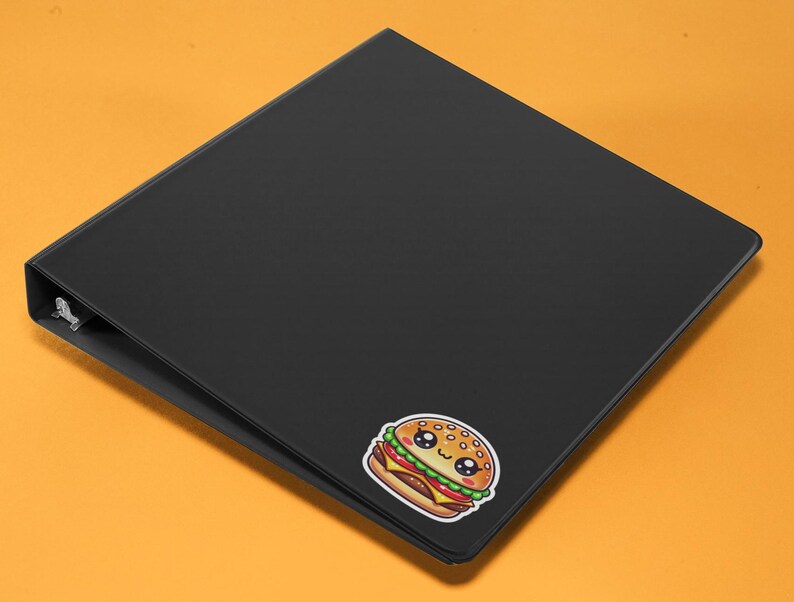 Pu&ograve; includere: Un raccoglitore nero con un adesivo di hamburger di cartone animato carino. L'hamburger ha un viso sorridente ed &egrave; decorato con semi di sesamo.