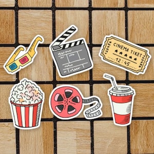 May include: A set of six colourful stickers featuring movie-themed imagery. The stickers include a pair of 3D glasses, a clapperboard, a film reel, a popcorn bucket, a soda cup, and a cinema ticket with the text "CINEMA TICKET" and "12:45".