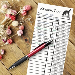 May include: A reading log with the title "Reading Log" and the name "Lola Lewis" is displayed on a wooden surface. A red and black pen rests on the log, next to a bouquet of dried flowers. The log includes book titles and a rating section.