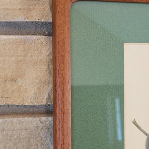 May include: Close-up of the top right corner of a wooden picture frame. The frame is a rich brown color and has a slightly textured surface. The inside of the frame is lined with a green mat.