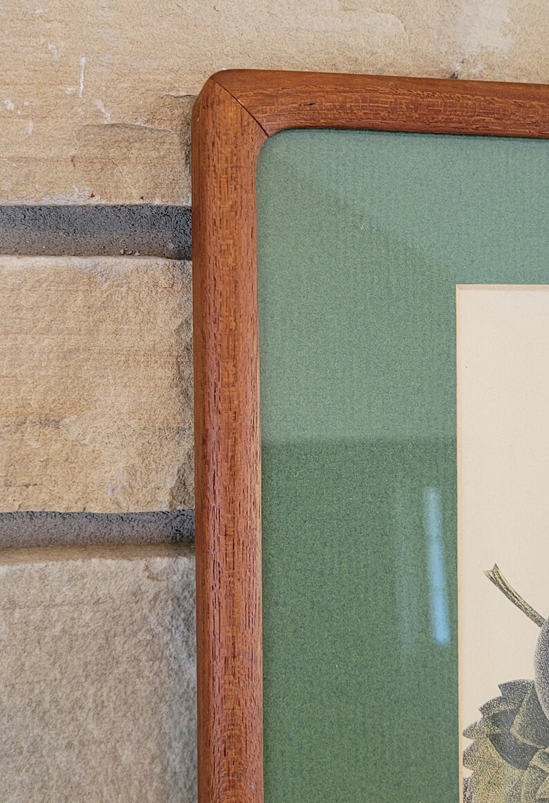 May include: Close-up of the top right corner of a wooden picture frame. The frame is a rich brown color and has a slightly textured surface. The inside of the frame is lined with a green mat.
