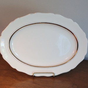 Puede incluir: Plato ovalado blanco para servir con borde dorado. El plato tiene un borde festoneado.
