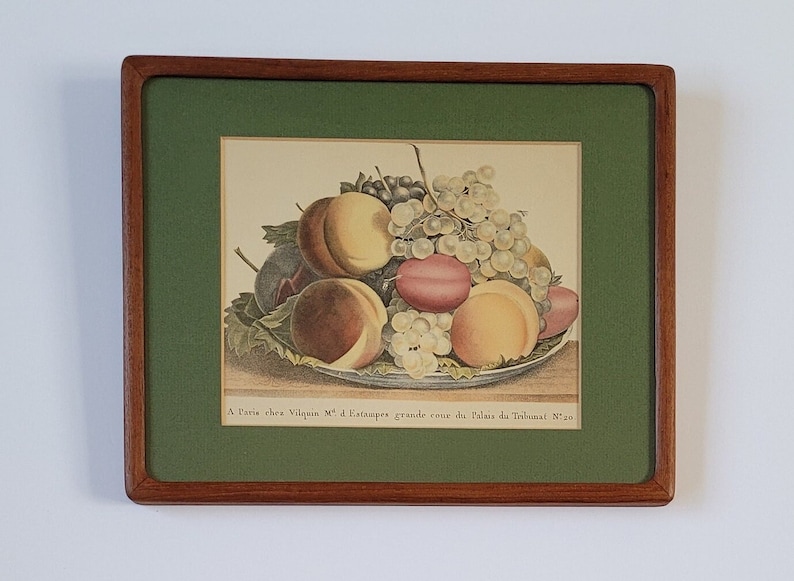 May include: A framed print of a still life featuring a bowl of fruit. The bowl contains peaches, plums, and grapes. The print is titled "A Paris chez Viquien N&deg; d'Estampes grande cours du Palais du Tribunat N&deg; 30".