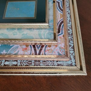 May include: A set of three picture frames with gold trim and intricate patterned paper mats. The frames are nested within each other, creating a layered effect.