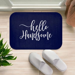 May include: A navy blue bath mat with white text that reads "hello handsome".