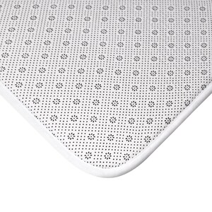 May include: Close-up of a white rug corner with a black floral pattern on a dotted background. The rug has a white border and a non-slip backing.
