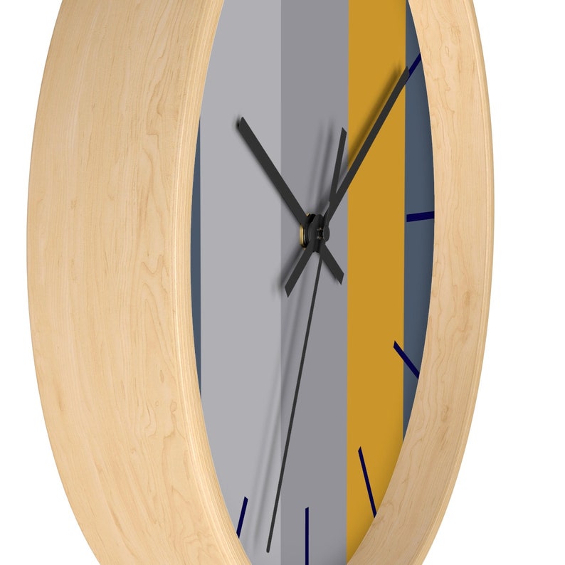 Puede incluir: Un reloj de pared redondo con marco de madera clara. La esfera del reloj est&aacute; dividida en franjas verticales grises, amarillo mostaza y azul marino. Las manecillas negras y los marcadores azules indican la hora.