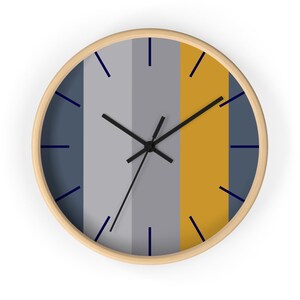 Puede incluir: Un reloj de pared redondo con marco de madera clara. La esfera del reloj presenta rayas verticales en tonos azul, gris y dorado. Las manecillas negras y los marcadores de hora azul marino completan el dise&ntilde;o. Un elemento de decoraci&oacute;n del hogar moderno y minimalista.