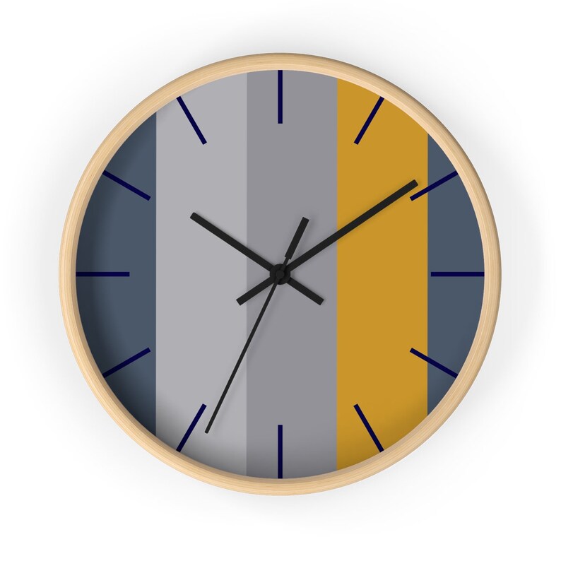 Puede incluir: Un reloj de pared redondo con marco de madera clara. La esfera del reloj presenta rayas verticales en tonos azul, gris y dorado. Las manecillas negras y los marcadores de hora azul marino completan el dise&ntilde;o. Un elemento de decoraci&oacute;n del hogar moderno y minimalista.