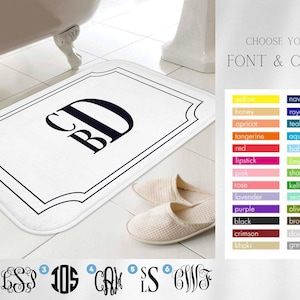 May include: White bath mat with a black border and a monogram in the center. The monogram is in a script font and reads "CB". The mat is shown on a bathroom floor with a white bathtub in the background. The image also shows a color chart with different font styles and colors to choose from.