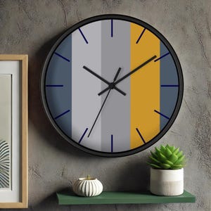 Puede incluir: Un reloj de pared redondo con marco negro y esfera a rayas de colores. La esfera presenta rayas verticales en azul, gris y amarillo. Las manecillas del reloj son negras y los marcadores de hora son azules. Un reloj decorativo moderno.