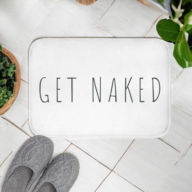 Może przedstawiać: Biała mata łazienkowa z nadrukiem "GET NAKED" w kolorze czarnym.