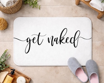 May include: A rectangular white bath mat featuring the black cursive text get naked centred on the surface. The mat has rounded corners and a soft texture, providing a clean and simple design for a bathroom floor space.