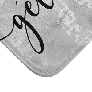 May include: A gray and white bath mat with the word "together" in black script. The mat has a textured, watercolor-like background. The corner of the mat is visible, showing a rounded edge.