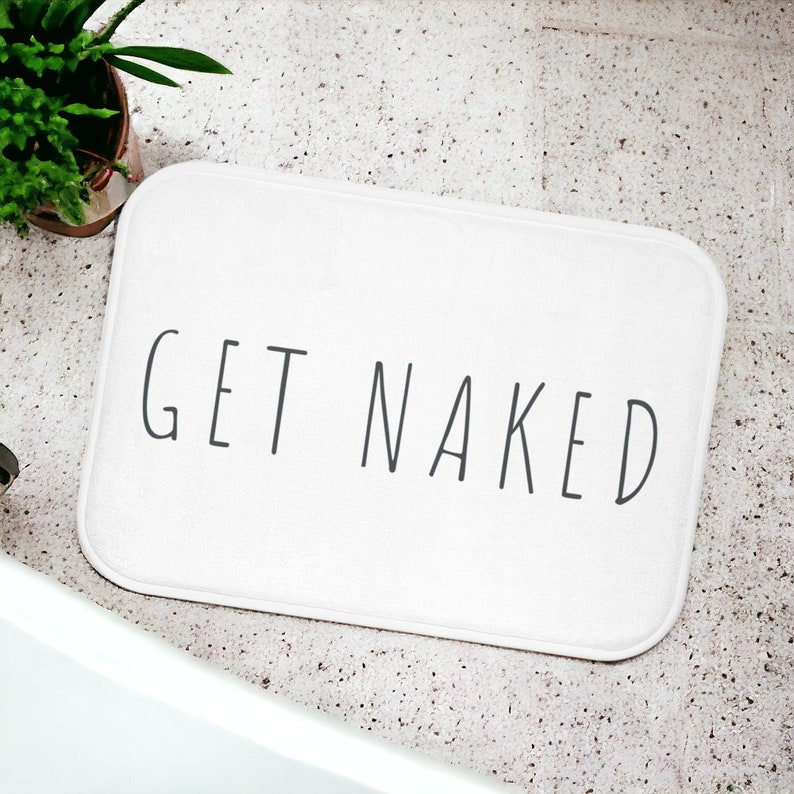 Może przedstawiać: Biała mata łazienkowa z nadrukiem "GET NAKED" w kolorze czarnym.