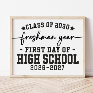 May include: A framed print with the text "CLASS OF 2030 freshman year - FIRST DAY OF - HIGH SCHOOL 2026-2027" in black lettering. The frame is a light wood colour, and the background is white.