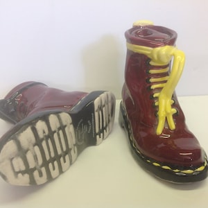 May include: Two red ceramic boots with yellow laces. One boot is shown from the side and the other is shown from the bottom.