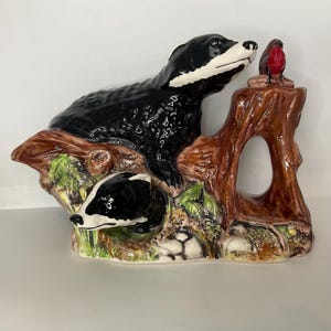 May include: A ceramic figurine featuring two black and white badgers on a brown tree trunk with a red-breasted bird. The figurine has green foliage and is painted with glossy black and brown colors.