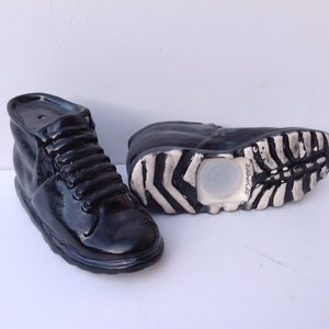 May include: A pair of black ceramic salt and pepper shakers shaped like boots. The shakers have a white rubber bottom and a small hole on the top for pouring.