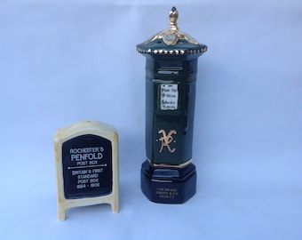 May include: A green ceramic replica of a British post box with gold accents and a sign that reads "Rochester's Penfold Post Box Britain's First Standard Post Box 1854-1905".