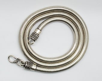 Può includere: Una collana a catena di serpente d'argento con chiusura a moschettone. La catena è realizzata con piccoli anelli intrecciati che creano un aspetto liscio e fluido.