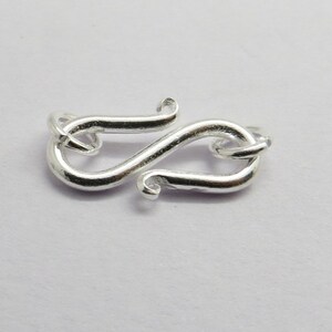 Puede incluir: Cierre de metal plateado con un dise&ntilde;o decorativo en forma de S estilizado. El cierre est&aacute; dise&ntilde;ado para la elaboraci&oacute;n de joyas.
