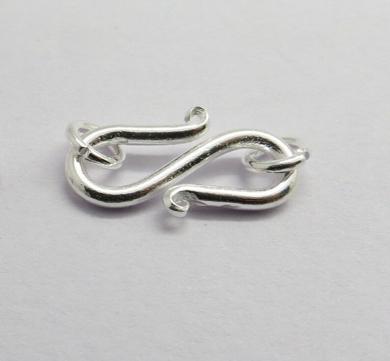 Puede incluir: Cierre de metal plateado con un dise&ntilde;o decorativo en forma de S estilizado. El cierre est&aacute; dise&ntilde;ado para la elaboraci&oacute;n de joyas.