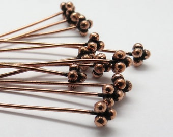 May include: A group of copper head pins with a cluster of small round balls at the end of each pin.