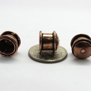 May include: Three copper-colored metal beads, each with a different design. The beads are about the size of a US dime.