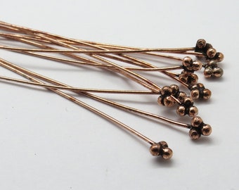 May include: A bunch of copper-colored head pins with a cluster of small balls at the end. The pins are arranged in a fan shape.