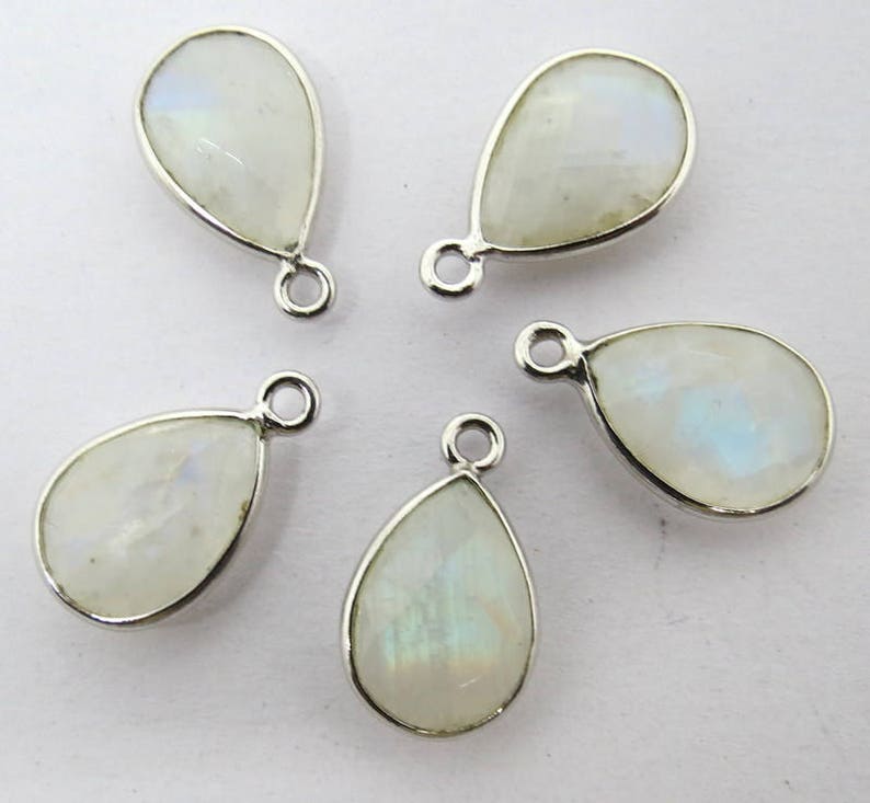 May include: Five silver teardrop-shaped pendants with white moonstone gemstones. Each pendant has a small loop at the top for attaching to jewelry.
