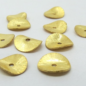 May include: A collection of nine gold-coloured metal beads with a hole in the centre. The beads are shaped like a leaf and have a textured surface.