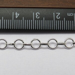 Op de afbeelding: Een close-up van een zilveren ketting met ronde schakels. De ketting wordt gemeten met een liniaal, wat laat zien dat elke schakel ongeveer 5 mm in diameter is.