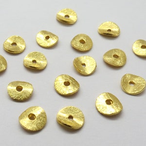 Peut inclure: Un ensemble de 15 perles en métal doré avec une finition texturée. Chaque perle a une forme circulaire avec un trou au centre.