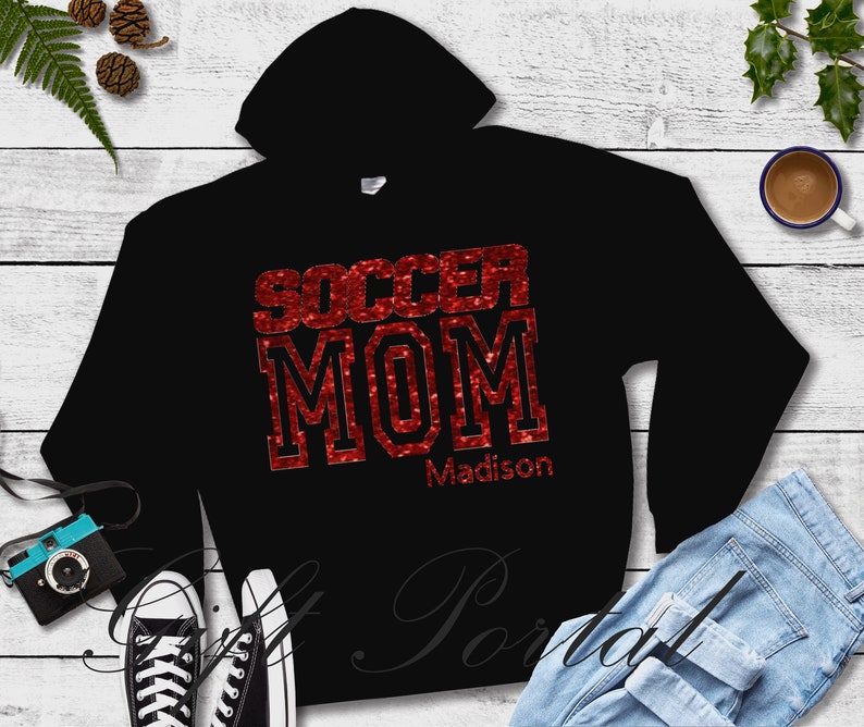 May include: Black hoodie with red glitter text that says "Soccer Mom" and the name "Madison" underneath.