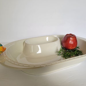 May include: White ceramic serving dish with a separate bowl in the center. The dish has a decorative rim with small dots and a fish figurine handle. An apple is sitting on the dish.