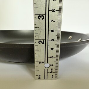 Puede incluir: Una sart&eacute;n gris oscuro con un mango negro. La sart&eacute;n tiene aproximadamente 5 cm de profundidad. Se coloca una regla met&aacute;lica junto a la sart&eacute;n para mostrar la profundidad.