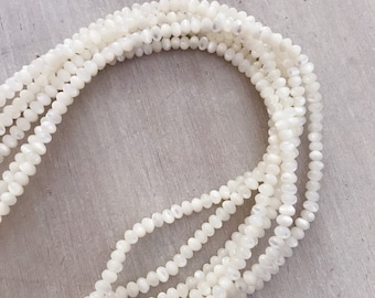 May include: A strand of white iridescent shell beads. The beads are round and have a slightly irregular shape. The beads are strung on a clear thread.