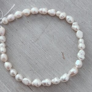 May include: A necklace of white, irregularly shaped freshwater pearls. The pearls are strung together, forming a circular shape. The pearls have a lustrous, creamy white colour and vary in size and shape.