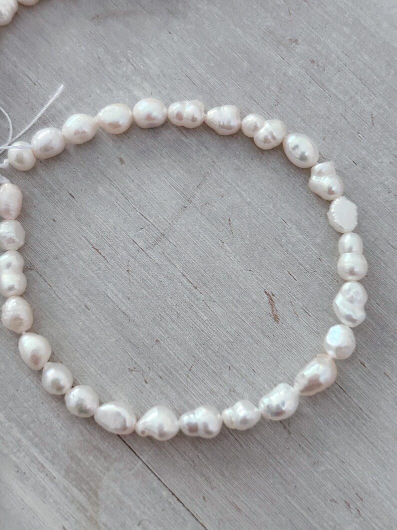 May include: A necklace of white, irregularly shaped freshwater pearls. The pearls are strung together, forming a circular shape. The pearls have a lustrous, creamy white colour and vary in size and shape.