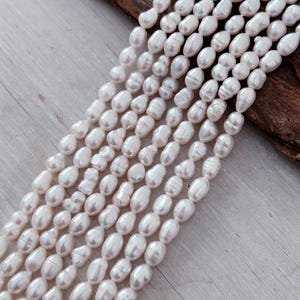 May include: Several strands of creamy white oval pearls. The pearls are strung together, creating a flowing, elegant appearance. The background features a wooden surface.