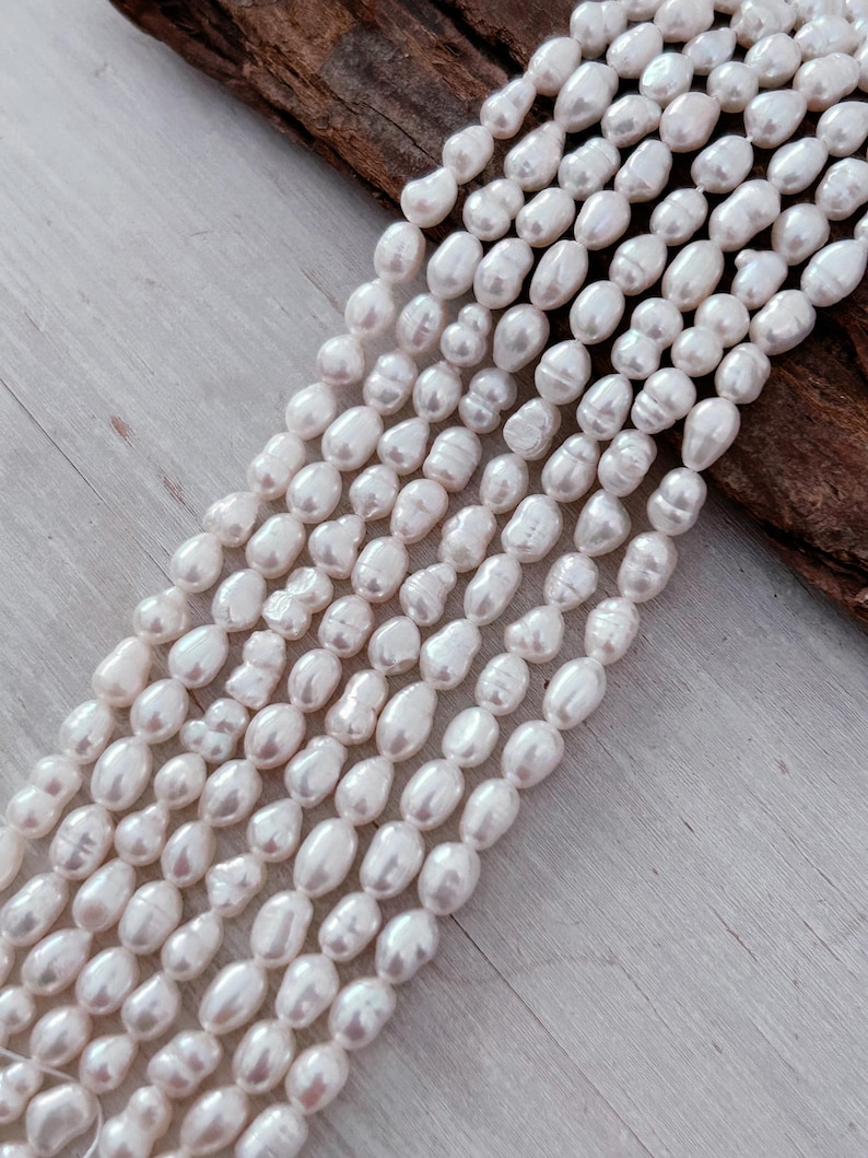 May include: Several strands of creamy white oval pearls. The pearls are strung together, creating a flowing, elegant appearance. The background features a wooden surface.