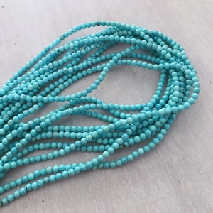 May include: A strand of turquoise beads, approximately 4mm in diameter, arranged in a loose coil on a light grey surface.