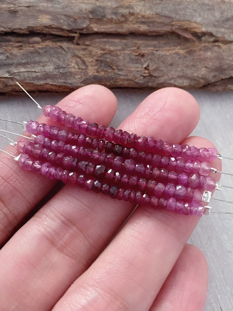 May include: A strand of pink ruby beads, faceted and strung on wire. The beads are small and uniform in size, and the strand is approximately 16 inches long.